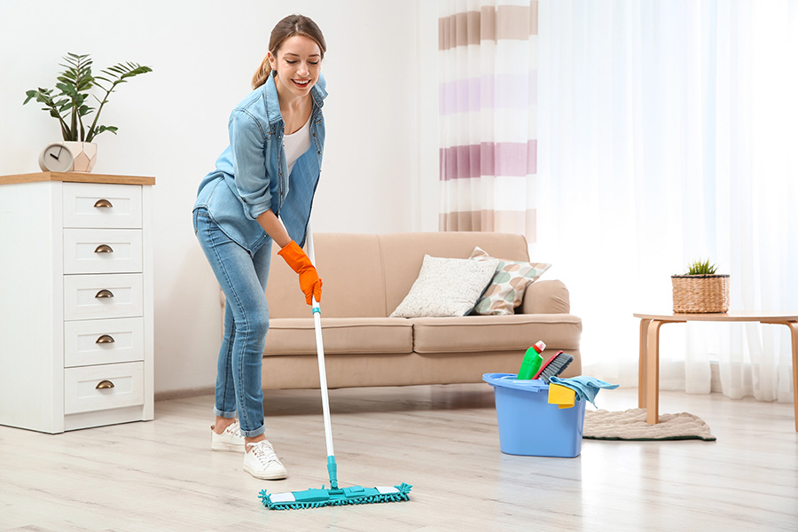 Eine Frau wischt im Wohnzimmer den Boden nass auf.