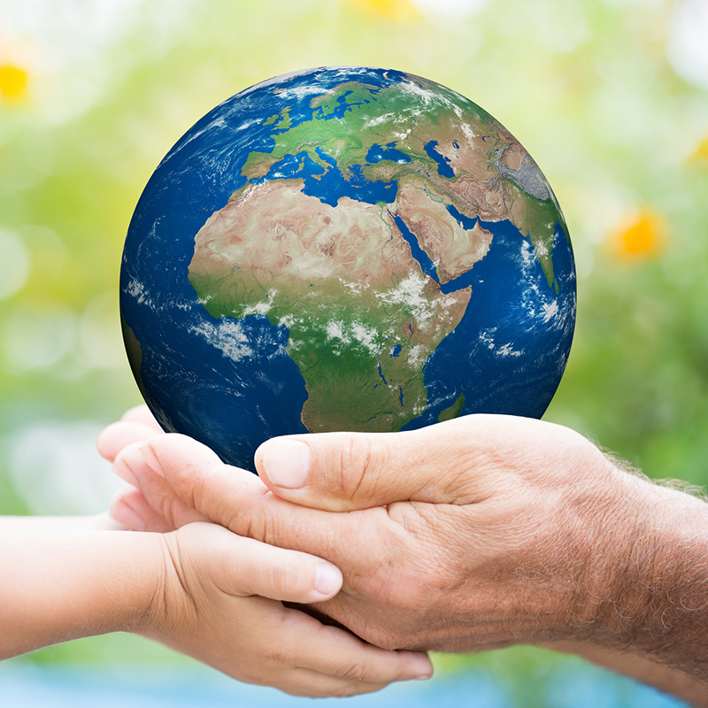 Child and senior man holding planet Earth in hands against green spring background. Elements of this image furnished by NASA