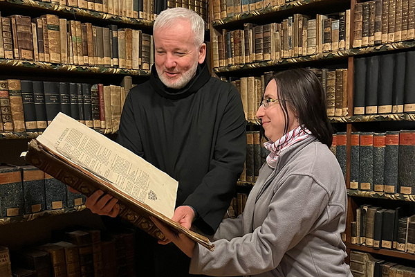 Frater Martin Macek und eine Archivarin blättern in einer Bibliothek in historischen Dokumenten. 